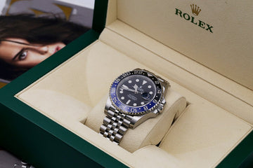 Image of a Rolex Batman model inside a green Rolex box with tan fabric inside, whilst the watch itself has a stainless steel case and bracelet to match, both featuring high-polished and satin-finished accents.
